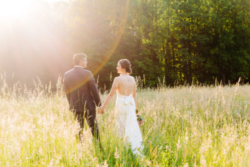 Light hits bride and groom strolling in a field