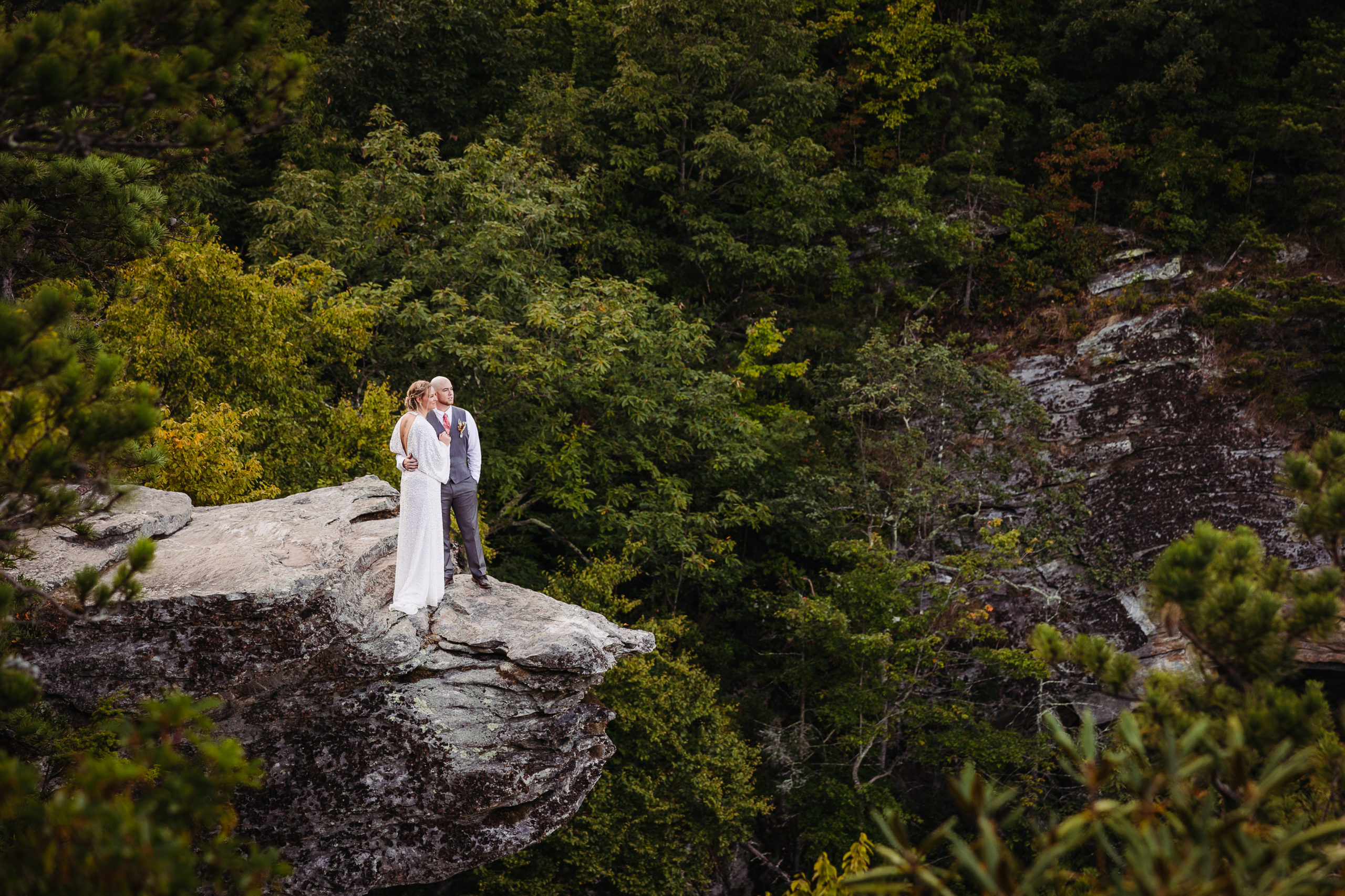Couple stands on edge of rock overlooking mountains elopement