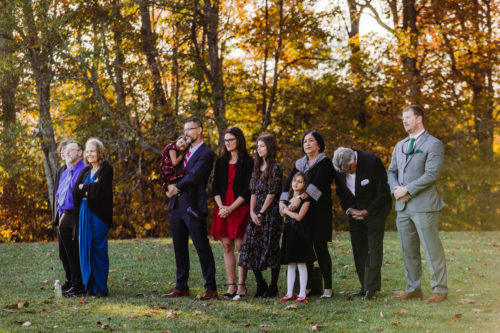 A group of adults and children huddle together watching a wedding elopement ceremony