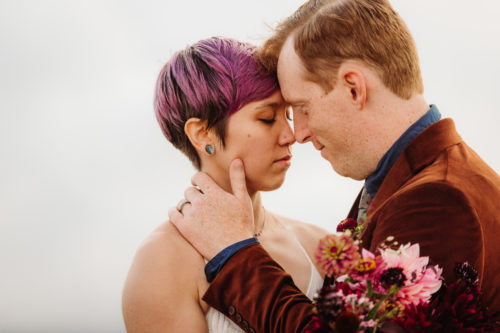 White woman with purple hair touches forehead with white man with brown hair on their wedding 