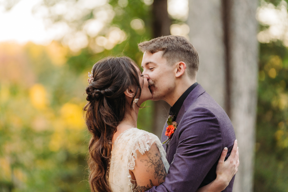 Couple kissing outdoors with lush greenery and soft autumn light in Asheville.