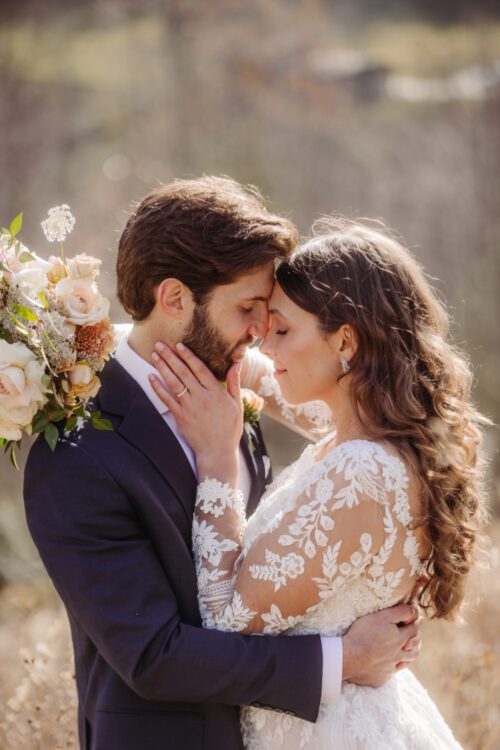 Couple embracing in a mountain landscape with bride holding a bouquet of soft florals.