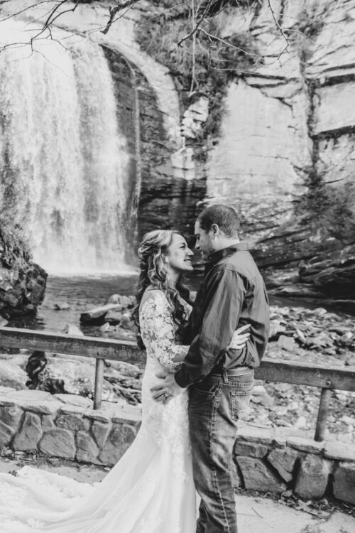 Couple standing in front of a waterfall, smiling at each other, captured in black and white.