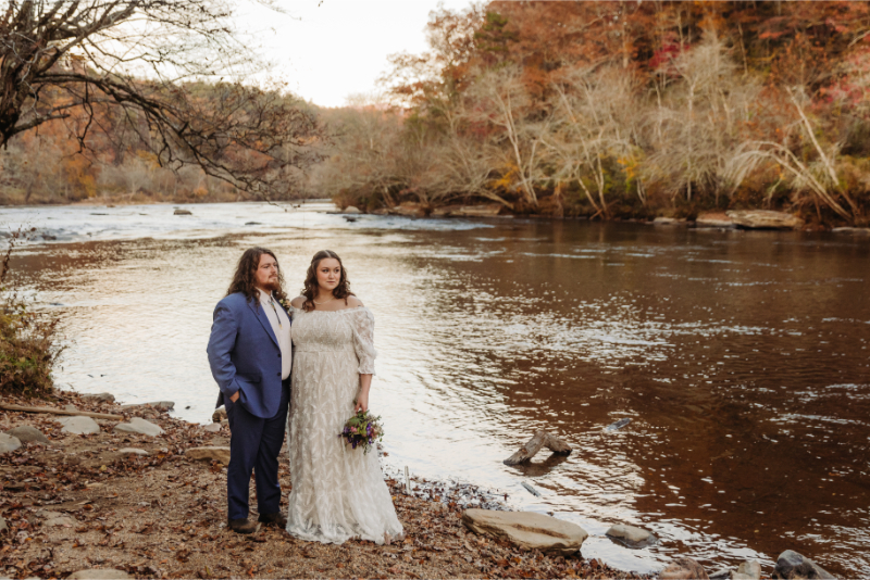 Bride and groom stand in front of North Carolina creek setting as an all-inclusive outdoor elopement planner helps them coordinate their elopement.