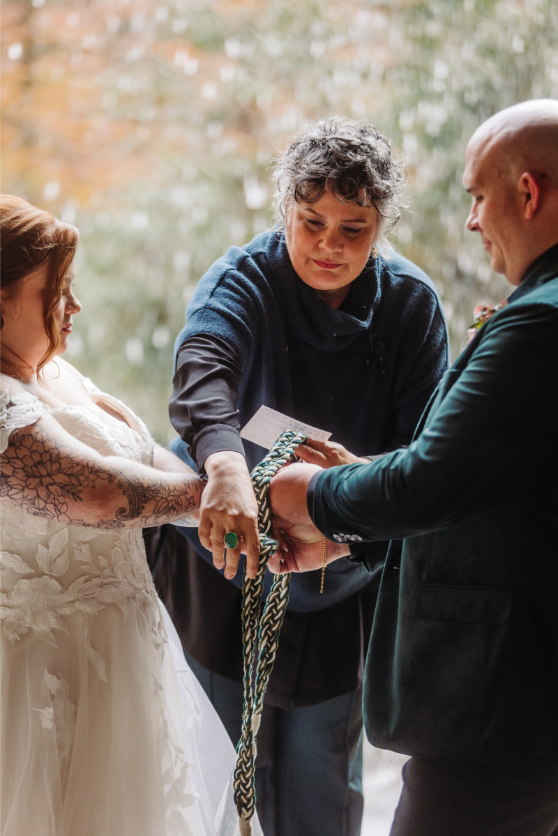 All-inclusive outdoor elopement planner ties knot around couple's hand during ceremony.