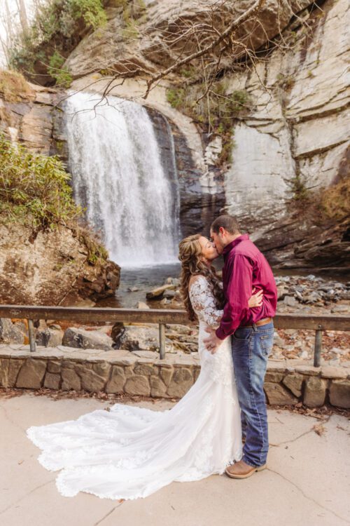 bride and groom kiss outdoors with a waterfall in the background