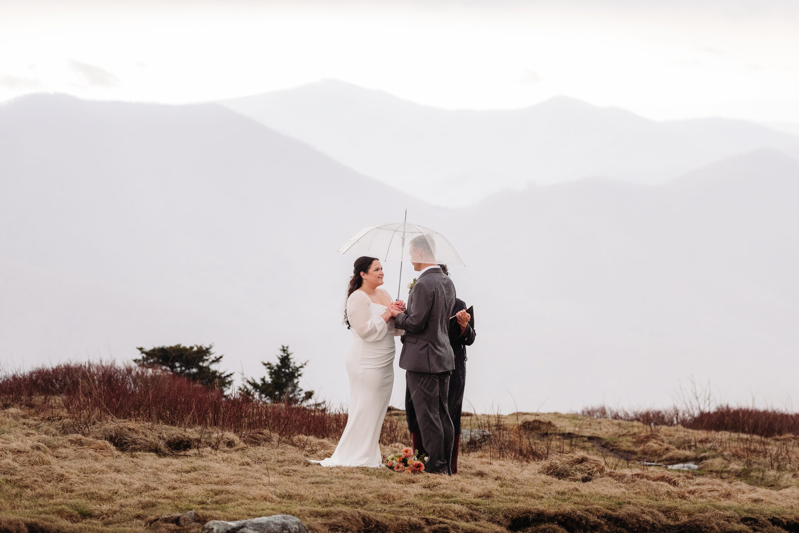 Eloping couple exchanging vows under a clear umbrella as rain gently falls during their intimate outdoor ceremony