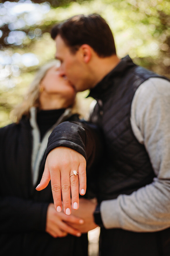 Couple kisses as woman shows engagement ring close to camera.