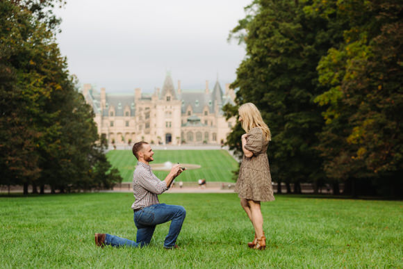 Man kneels to propose on Biltmore Estate lawn.