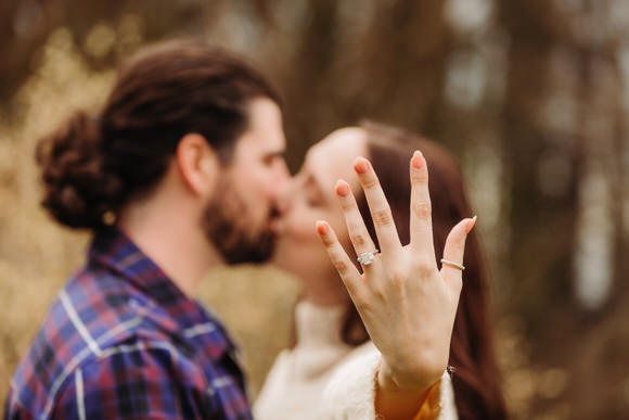 Couple kisses while showing engagement ring to camera.