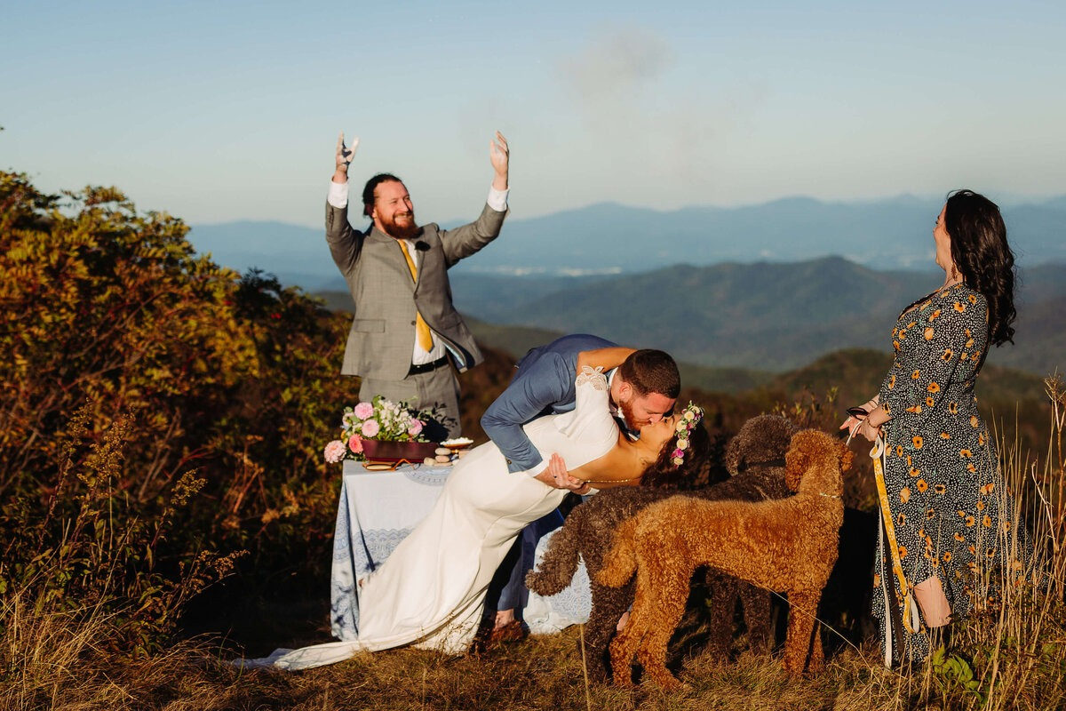 Bride and groom share a mountain-top kiss with dogs present, coordinated by our Vendor Dream Team in Asheville.