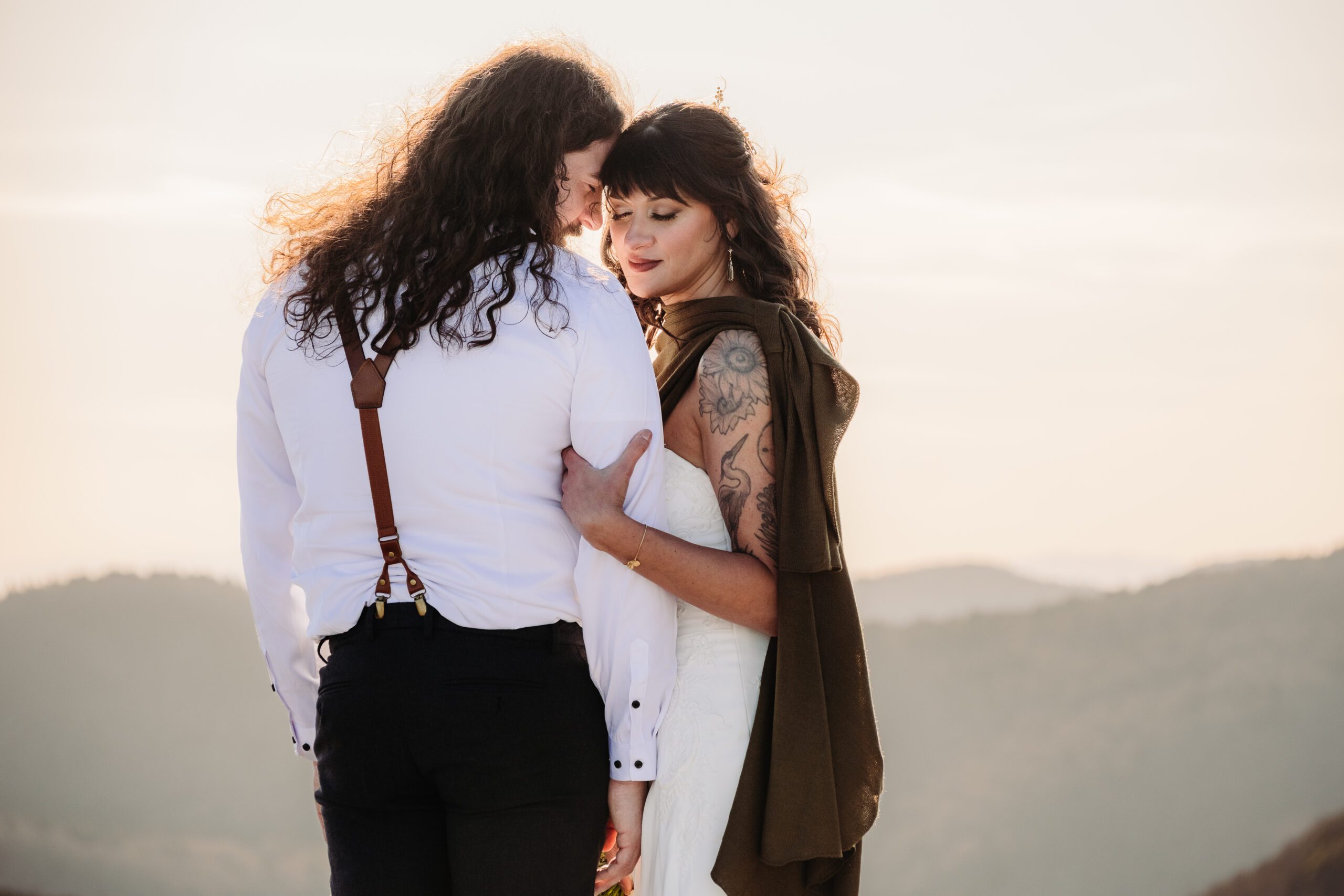 Couple embracing on mountain overlook at sunset, capturing love and elevating your elopement experience.