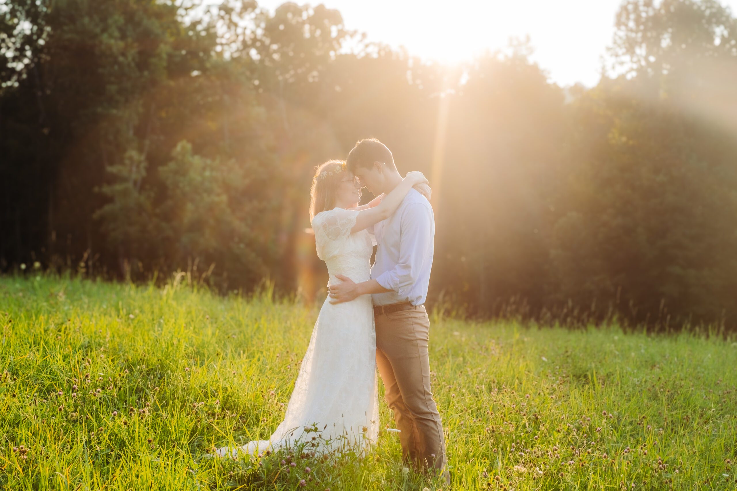 Bride and groom embrace in sunlit meadow, surrounded by golden light during their intimate ceremony.