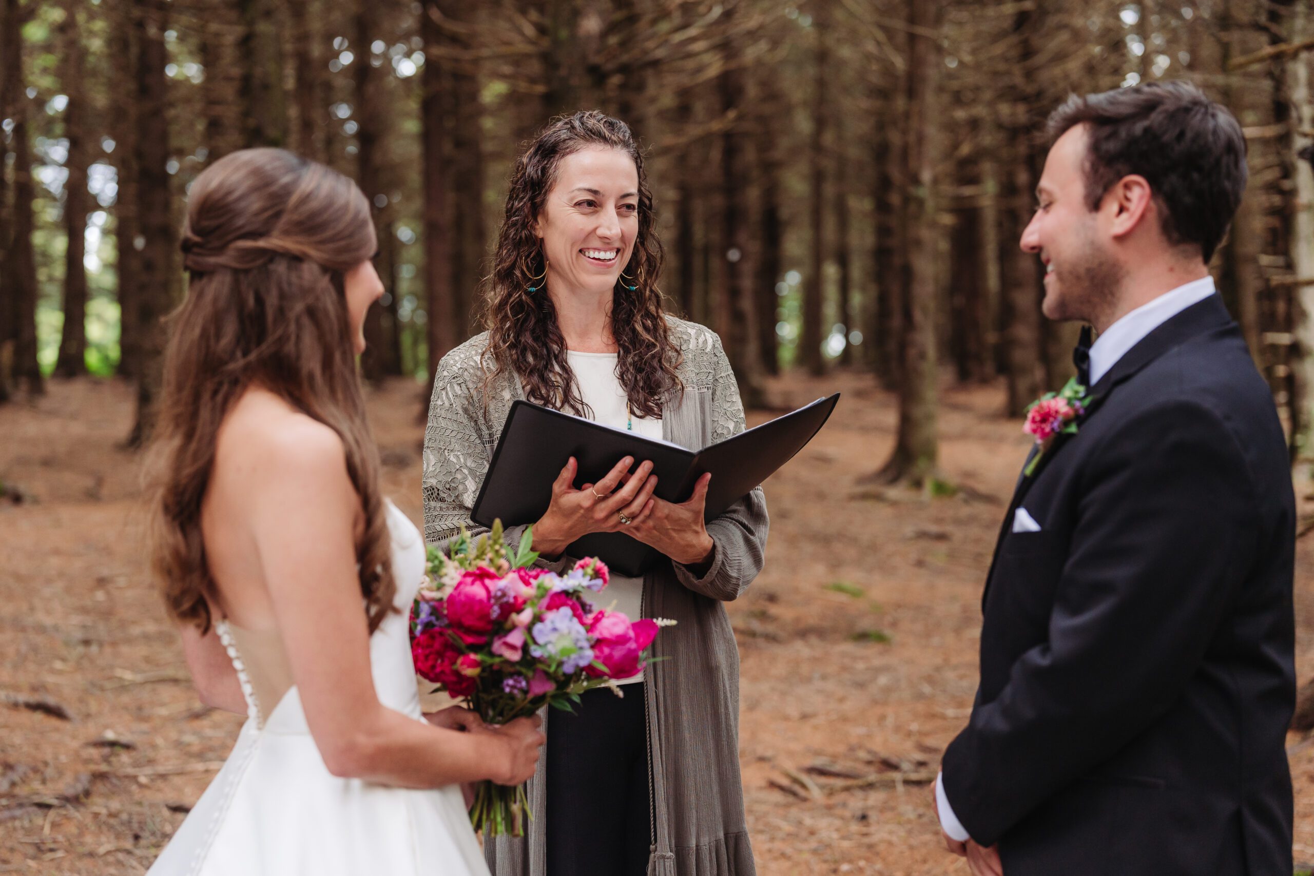 Bride and groom exchange vows with officiant in forest ceremony, beautifully elevating your elopement experience.