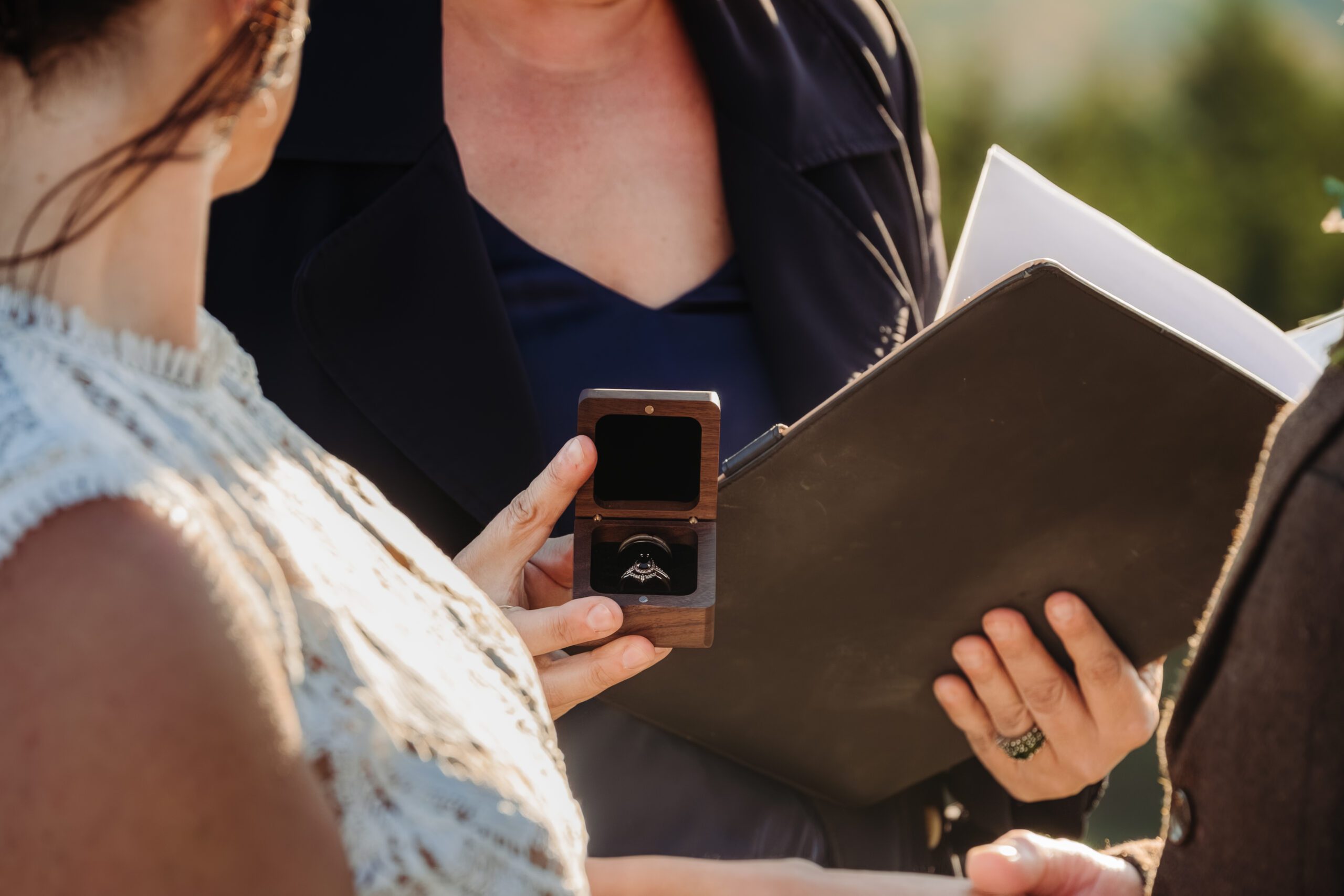 Officiant holds ring box during outdoor ceremony as couple prepares to exchange vows.