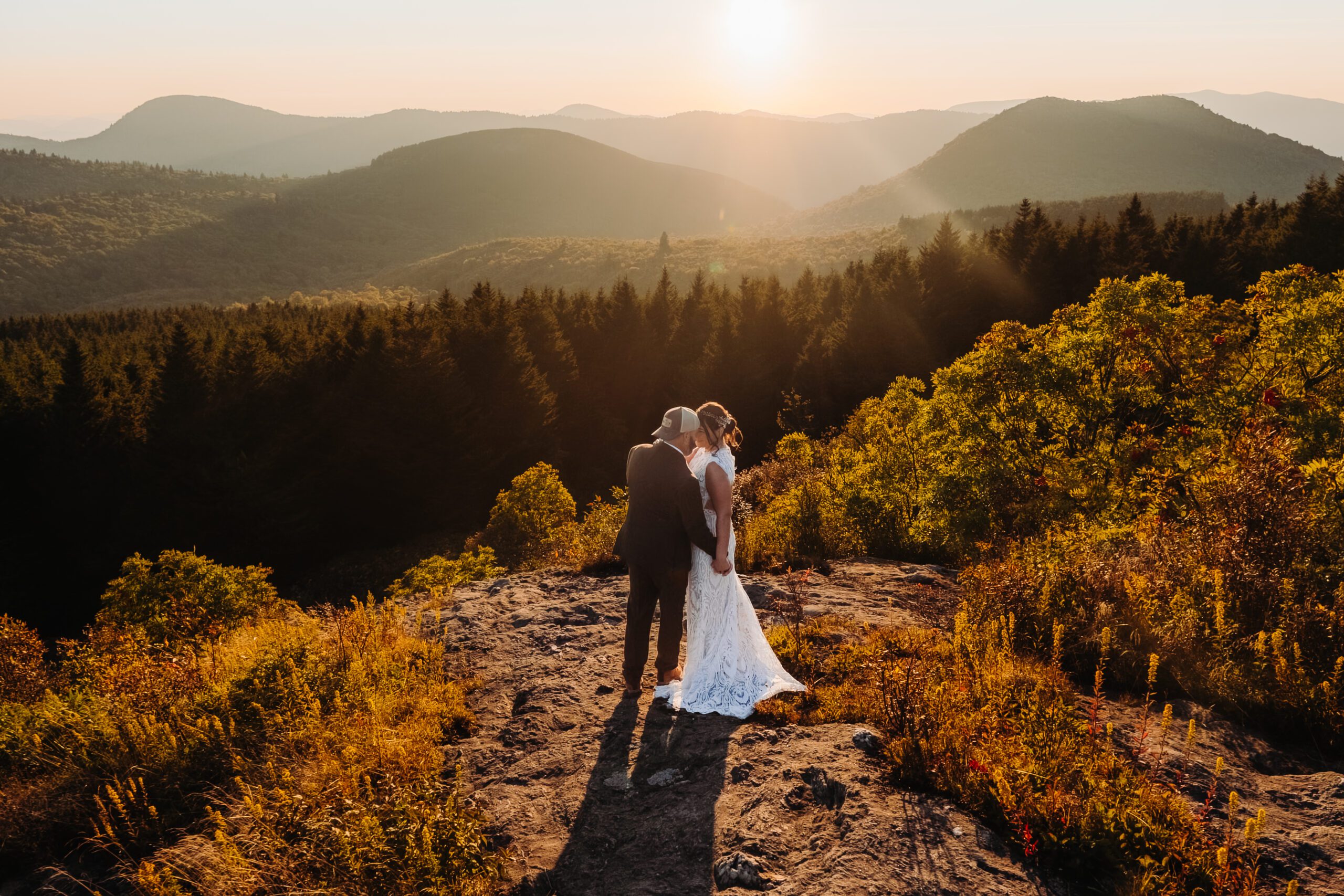 Couple embraces on mountain cliff at sunset in Asheville, enjoying romantic post-elopement adventures together.