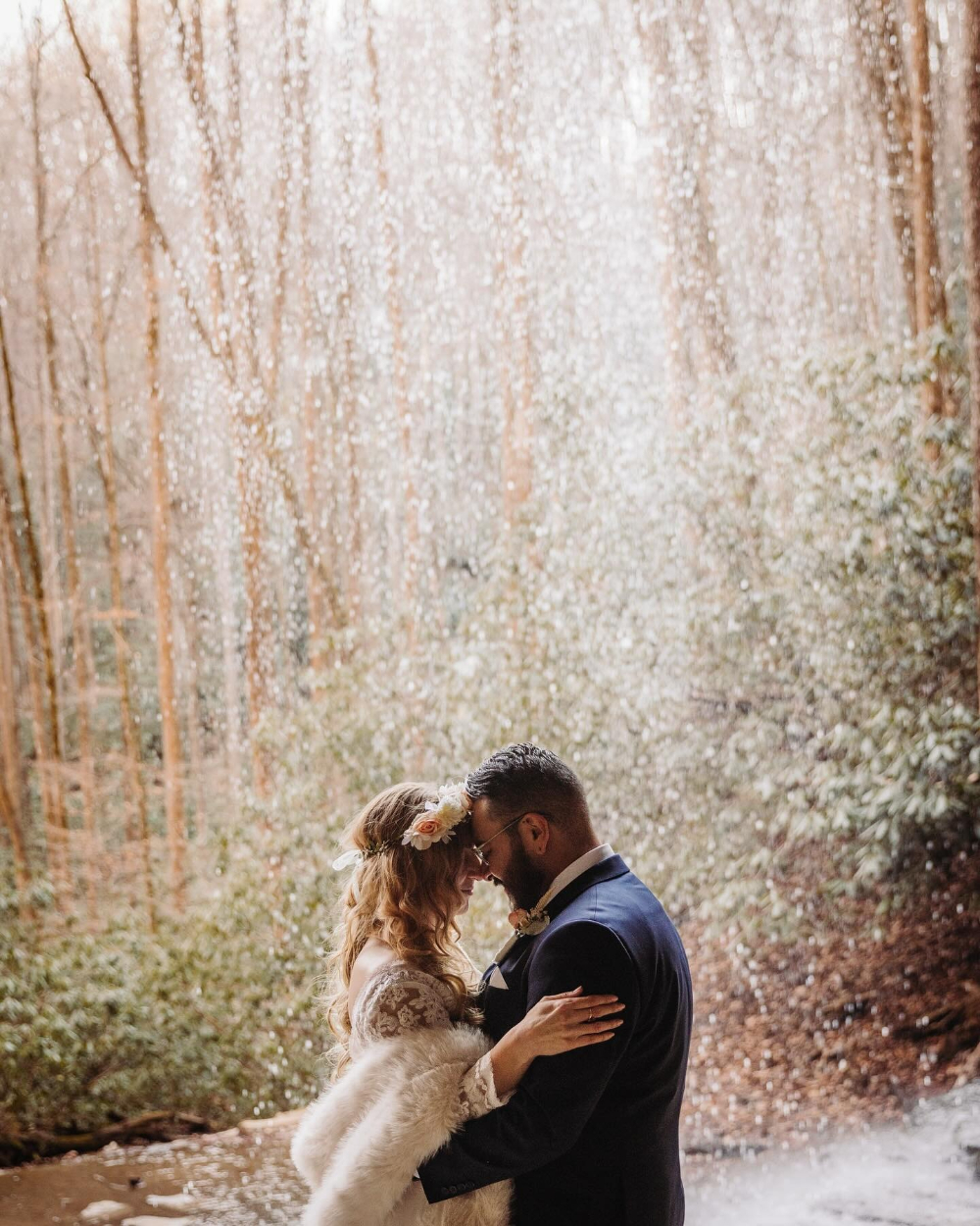 Bride and groom embrace under waterfall mist at one of Asheville’s hidden waterfalls in winter.