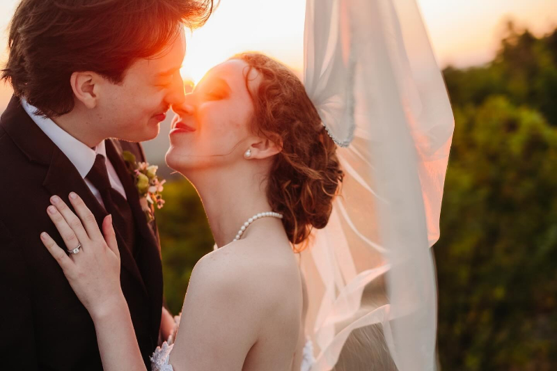 Couple sharing a sunset kiss with flowing veil during their day-after wedding photo session outdoors.