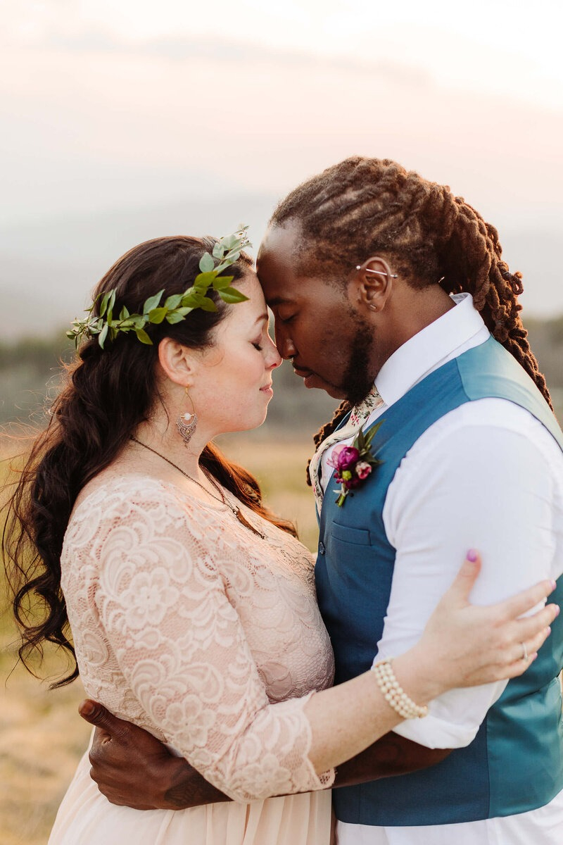 Couple embracing forehead to forehead at sunset, eyes closed, sharing an emotional and peaceful moment.