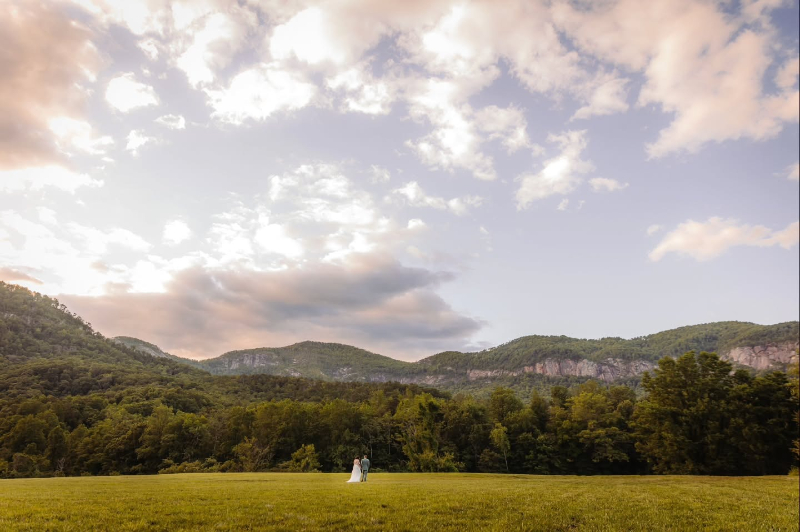 Couple stands in open field with mountain views in Asheville to renew their vows at sunset.