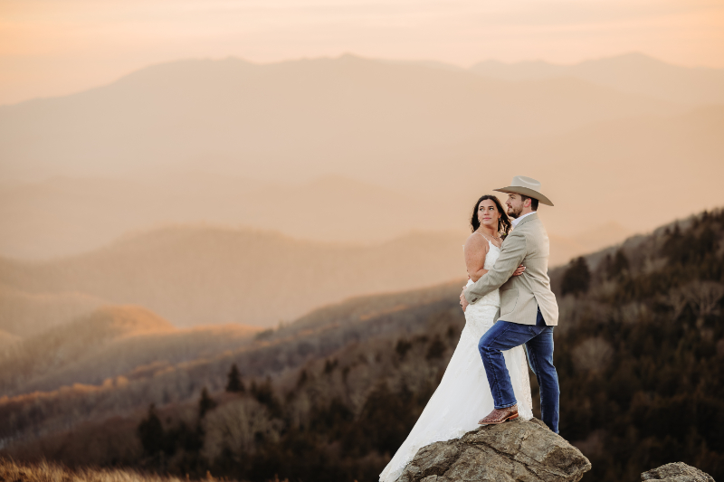 Couple stands on rocky peak with misty mountains behind them, creating a bold dream elopement backdrop.