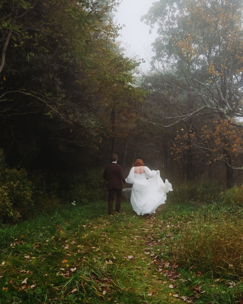 Couple walks through misty forest in wedding attire, a dreamy moment captured in elopement films.