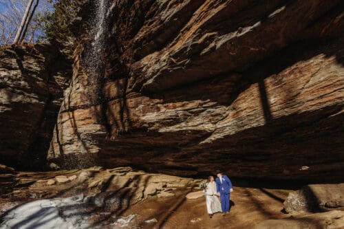 Couple stands beneath a rocky waterfall alcove, honoring nature and choosing to follow leave no trace principles.