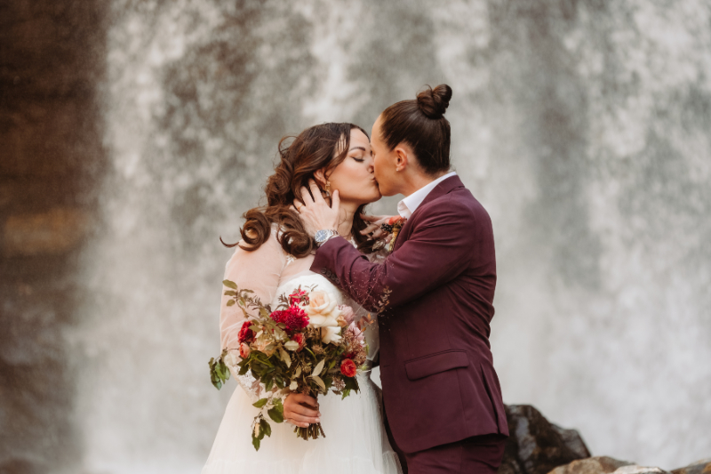 Couple kissing in front of waterfall with bouquet, following Leave No Trace principles during elopement.