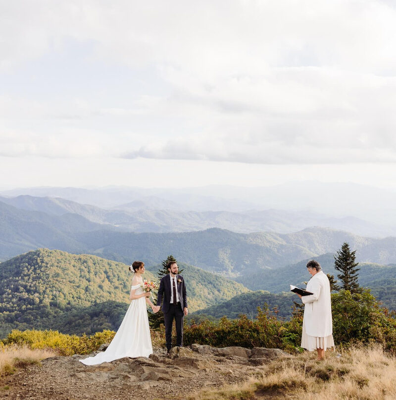 Couple exchanges vows on a mountain summit with sweeping views and an officiant by their side.