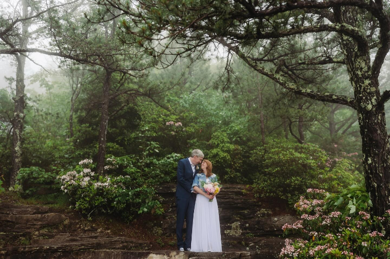 Couple shares a quiet moment in a misty forest, surrounded by soft pink mountain laurel blooms.