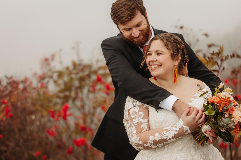 Couple embraces on a misty fall day, bouquet showing rich tones from our seasonal flower guide.
