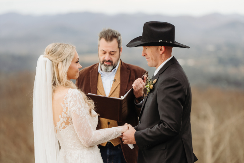 Bride and groom holding hands during intimate mountain ceremony with officiant.