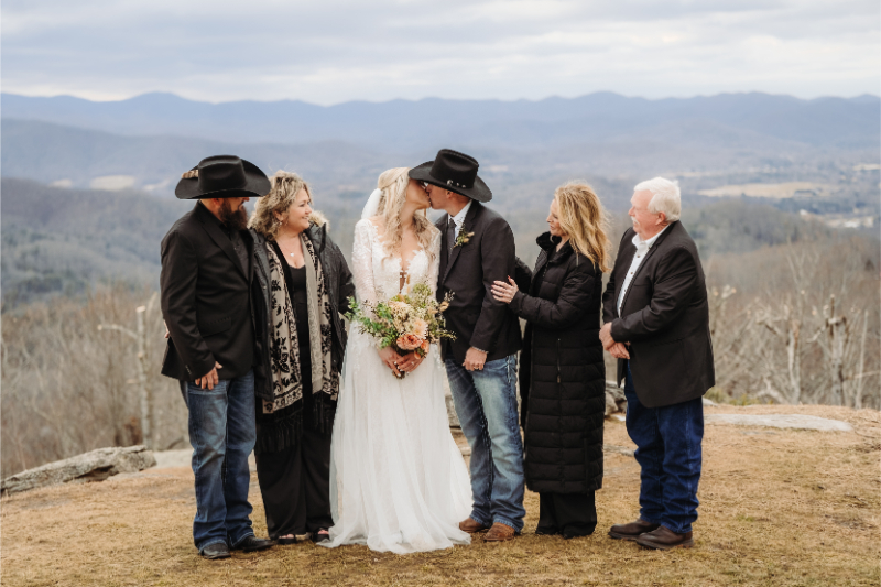 North Carolina mountain wedding couple kissing with family at scenic Blue Ridge overlook.
