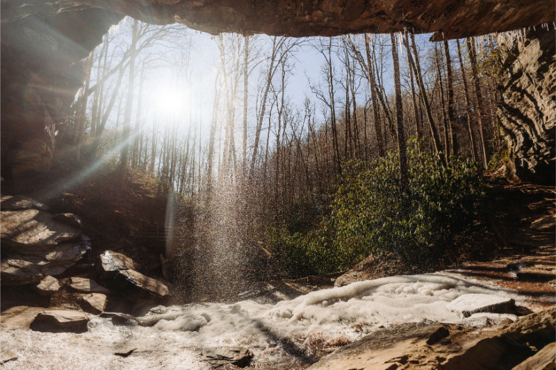 Sunlight streaming over waterfall during adventure in North Carolina forest elopement.