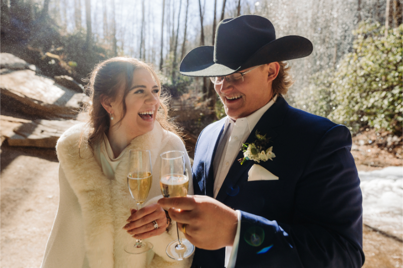 Couple toasting with champagne beside waterfall during adventure in North Carolina elopement.
