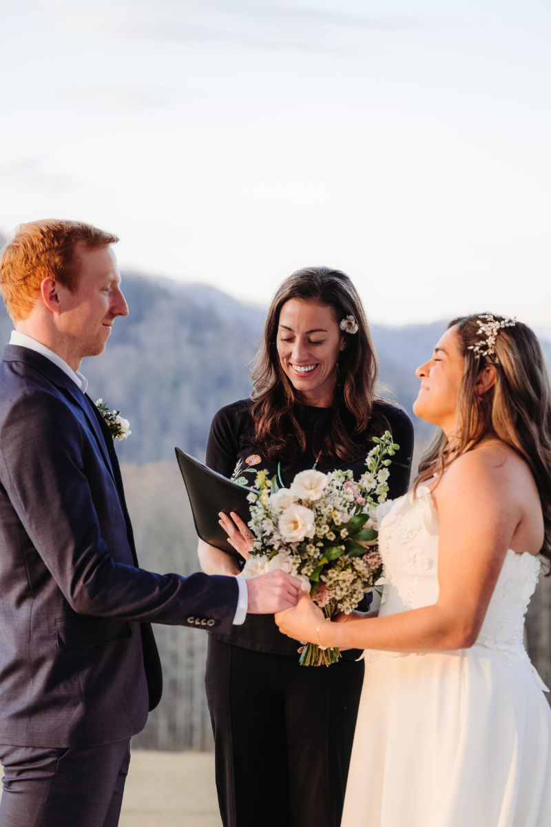 Couple holding hands during scenic mountain elopement ceremony with officiant and bouquet of flowers.
