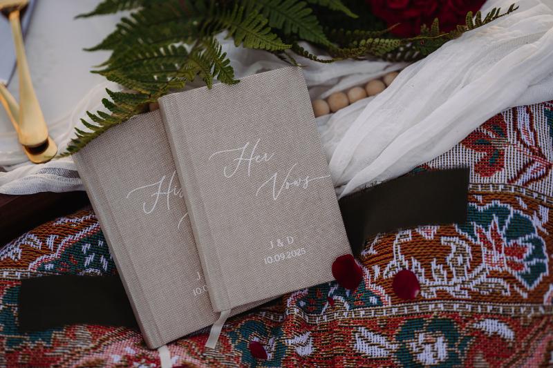 Elegant vow books placed on patterned blanket with greenery and fabric details for an intimate ceremony setup.