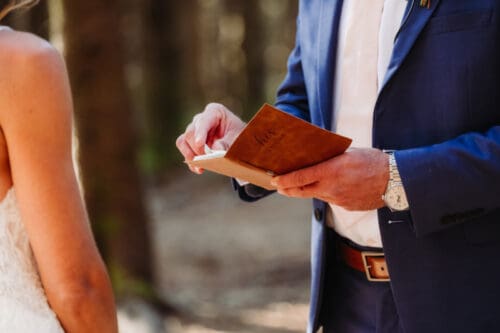 Officiant reading vows from a book during an intimate outdoor elopement ceremony in the forest.
