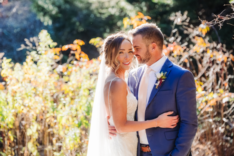 Smiling couple embracing in warm sunlight during outdoor elopement ceremony in a wildflower field.