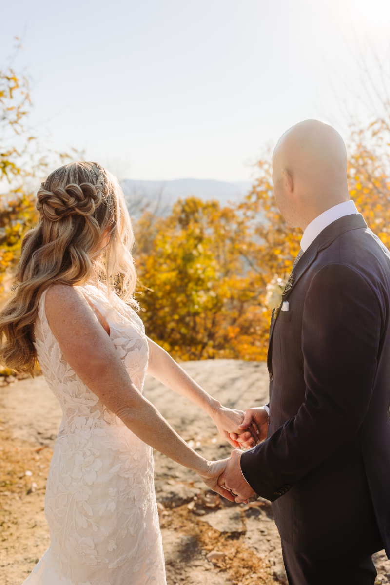 Couple holding hands at a scenic overlook, facing each other with mountains in the background