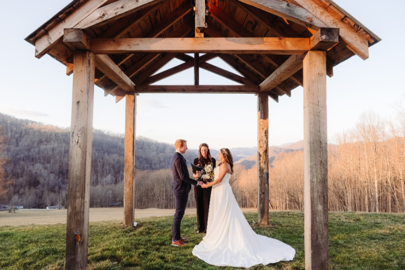 Couple standing under wooden arbor with mountain view, quiet and intimate outdoor ceremony moment