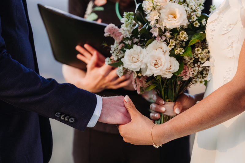 Couple exchanging bouquet during ceremony, soft florals and hands meeting in an intimate moment