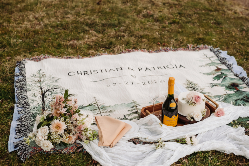 Couple’s picnic setup with blanket, flowers, and champagne for outdoor celebration