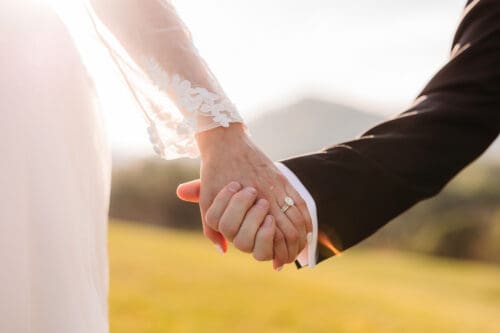 Bride and groom holding hands with engagement ring glowing in sunset light during Blue Ridge Mountain elopement