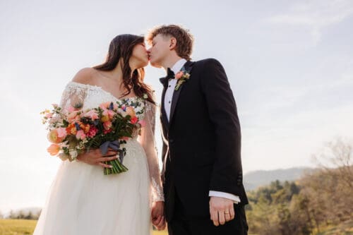 Bride and groom kissing at sunset with colorful bouquet during mountain elopement