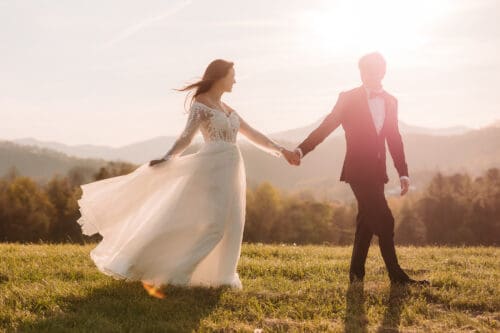 Bride and groom walking hand in hand at sunset in a glowing Blue Ridge Mountain field