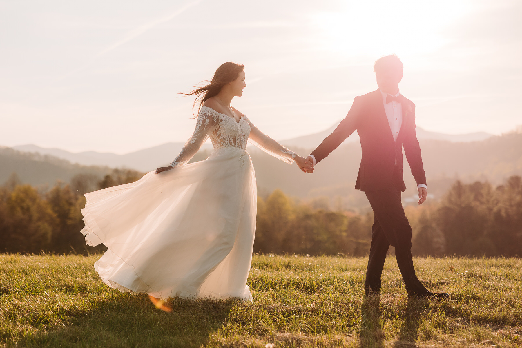 Bride and groom walking hand in hand at sunset in a glowing Blue Ridge Mountain field