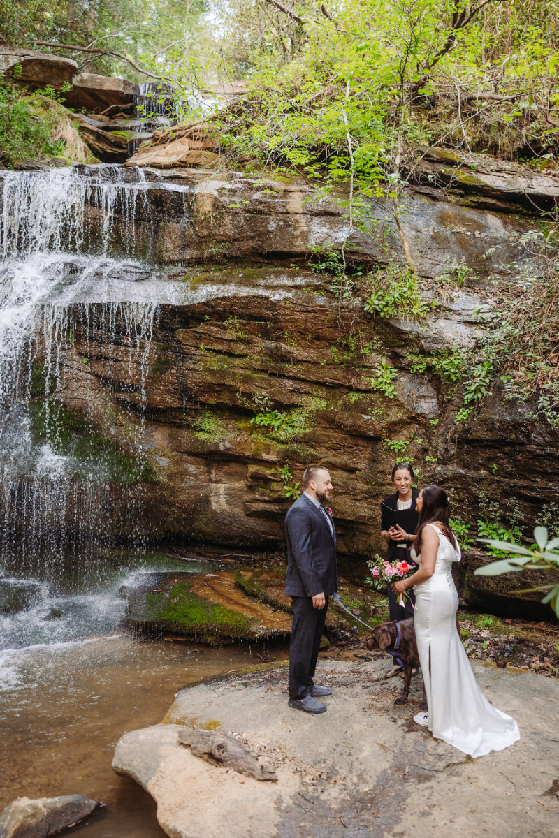 Couple exchanging vows at a waterfall elopement beside cascading falls and mossy rock backdrop