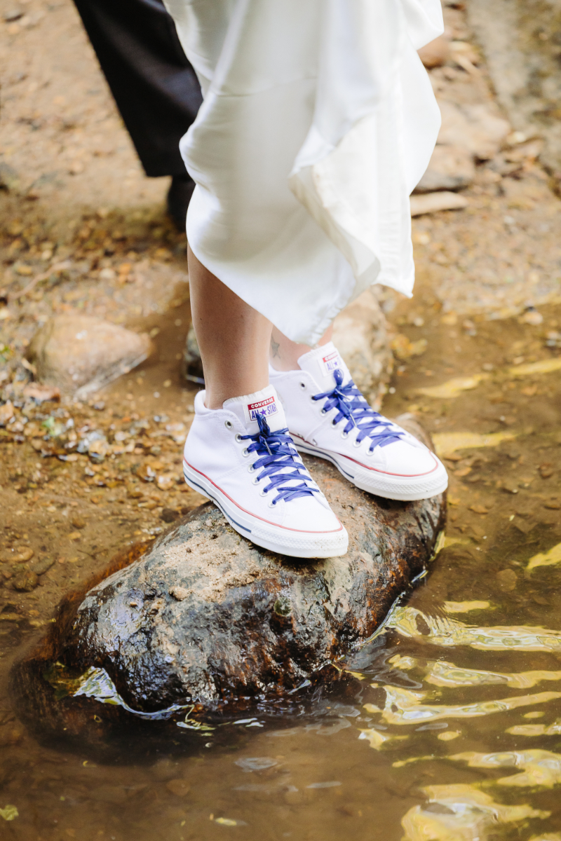 Bride in sneakers standing on rock in stream during waterfall elopement, blending style with adventure