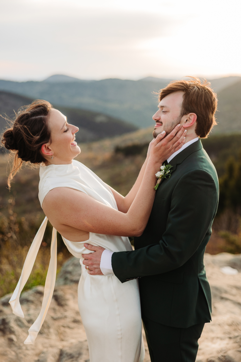 Bride and groom embracing and laughing together on a mountain overlook during their intimate wedding day.